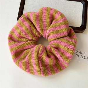 Pink and olive green striped knit scrunchie with soft woven texture on white desk