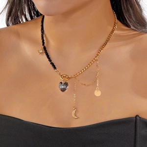Close-up of asymmetric necklace with crystal heart pendant and moon charm on a model