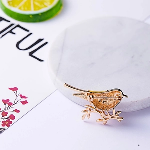 Detailed close-up of golden bird brooch with secure pin clasp on marble background