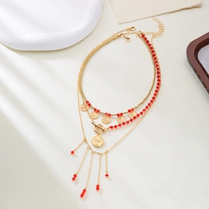 Détail de collier multicouche doré avec perles de cristal rouge et pendentifs pièces