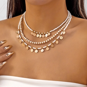 Détail d'un collier à trois couches de perles blanches et pendentifs pièces dorées