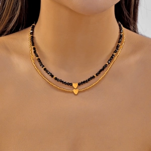 Double-layer necklace with black beaded strand and gold heart charms on a model's neck