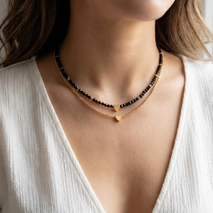 Close-up of double-layer necklace featuring black seed beads and golden heart pendants