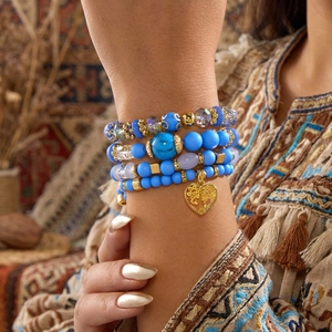 Details der mehrlagigen blauen Boho-Perlenarmbänder mit goldenem Herzanhänger am Handgelenk
