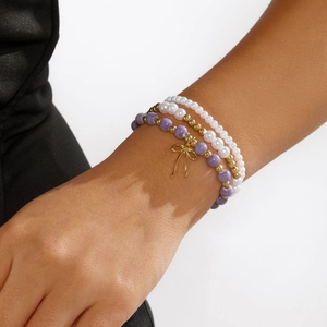 Detalle de set de tres pulseras bohemias con cuentas moradas y colgante de lazo dorado