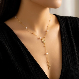 Detail einer goldenen Y-Halskette mit Perlen und Kreuzanhänger an einem Model