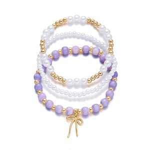Primer plano del set de cuatro pulseras con cuentas púrpuras, perlas y colgante de lazo dorado