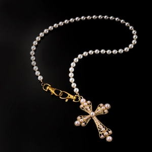 Macro detail of a pearl cross pendant with gold plating and white beads on black surface