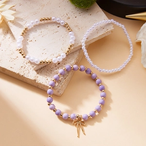 Detalle del set de tres pulseras de cuentas con perlas moradas y colgante de lazo dorado