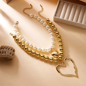 Detailed view of layered gold heart necklace with white pearls and chunky metallic beads