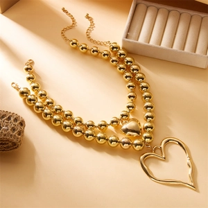 Detail of layered gold beaded necklace with irregular hollow heart pendant and lobster clasp