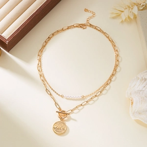 Détail d'un collier doré double épaisseur avec pendentif pièce, fermoir OT et petites perles