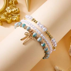 Detalle de tres pulseras de perlas con dije de lazo dorado sobre un soporte elegante