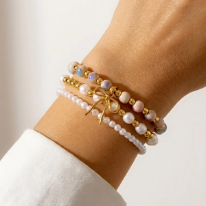 Primer plano de pulseras apiladas con cuentas de cerámica, perlas blancas y colgante de lazo