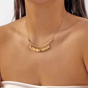 Détail d'un collier bohème vintage avec des breloques pièces gravées sur chaîne dorée