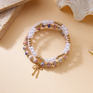 Detalle del conjunto de pulseras de perlas con colgante de lazo dorado en fondo elegante