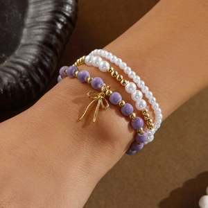 Conjunto de tres pulseras de perlas y cerámica con dije de lazo dorado en la muñeca