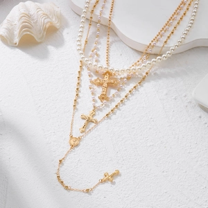 Détail d'un collier de perles multicouche avec pendentifs croix dorés sur un support blanc