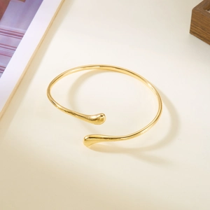 Vue détaillée d'un bracelet ouvert doré brillant au design moderne en forme de larme