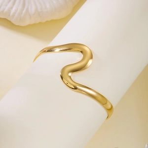 Détail d'un bracelet manchette doré poli en forme de vague sur un présentoir blanc