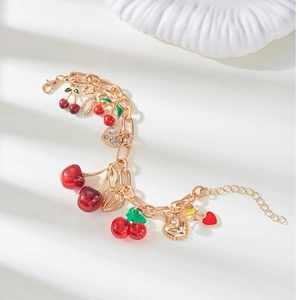 Detailed view of golden chain necklace with red cherry, heart charms and white faux pearls