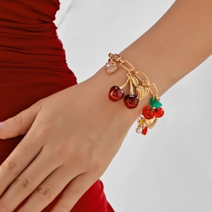 Detail of a gold chain bracelet with red cherry charms and crystal heart pendant on wrist