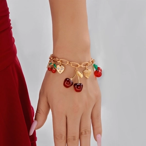 Detail of a gold-tone chunky chain bracelet with cherry and heart-shaped charms on a wrist