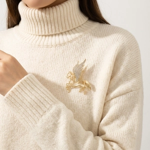 Close-up of luxury gold Pegasus brooch with crystal wings on cream knit sweater