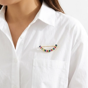Détail d'une broche courbée en or avec zircons multicolores sur une chemise blanche