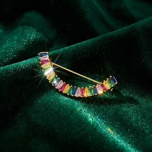 Détail macro d'une broche croissant avec zircons arc-en-ciel sur velours vert