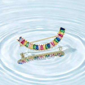 Détail d'une broche incurvée en zircons arc-en-ciel avec finition dorée sur l'eau bleue