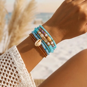 Detail of bohemian layered beads bracelet with sky blue accents and a natural seashell charm