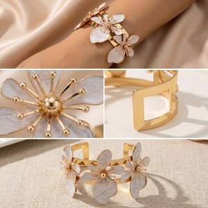 Dettaglio macro di bracciale rigido dorato con fiori in smalto bianco e pistilli metallici
