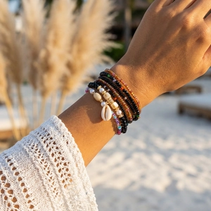 Detail of bohemian multilayer beaded bracelets with shell charm on a beach setting