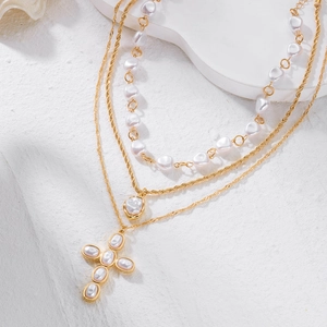 Détail de colliers multicouches dorés avec perles baroques et pendentif croix en perles