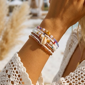Detail of layered bohemian bead bracelets with a natural shell charm on a model's wrist