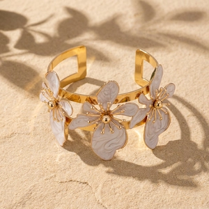 Dettaglio di un bracciale a polsino dorato con fiori in smalto bianco su pietra naturale
