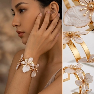 Dettaglio macro di un bracciale aperto boho dorato con fiori in smalto bianco e trame