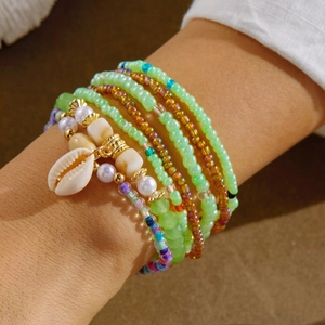 Detail of layered bohemian green bead bracelets with shell charm on model's wrist