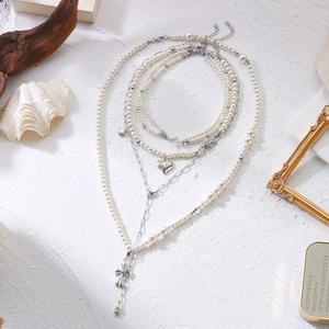 Détail de colliers de perles superposés avec croix en argent et pendentifs cœur sur fond