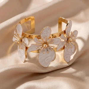 Dettaglio macro del bracciale aperto dorato con tre elementi floreali in smalto bianco