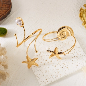 Dettaglio di bracciali dorati con stelle marine e perle su sfondo di pietra bianca