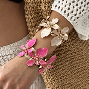 Dettaglio di motivi floreali in smalto rosa e crema su ampi bracciali dorati