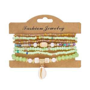 Detail of multi-layer beaded bracelet set in green and gold with a small shell charm