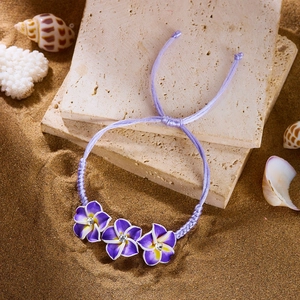 Böhmisches lila Plumeria Webarmband mit verstellbarer Kordel auf Strandsand-Hintergrund