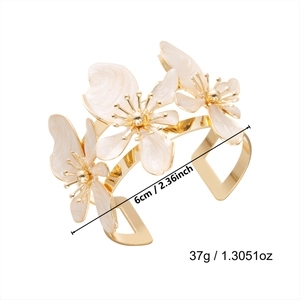 Dettaglio di un bracciale aperto dorato con fiori in smalto bianco e misura di 6 cm