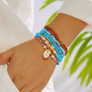 Detail of layered bohemian bead bracelets with shell charm and golden accents on wrist