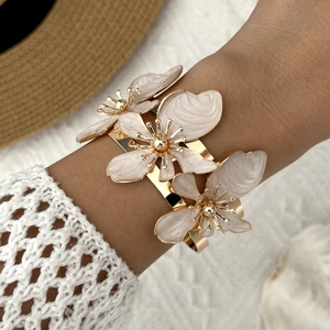 Dettaglio del bracciale rigido dorato con tre fiori in smalto bianco a rilievo in 3D
