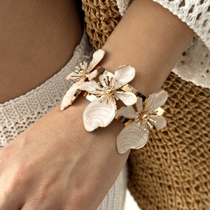Dettaglio di un bracciale dorato con tre fiori in smalto 3D bianchi sul polso di una modella