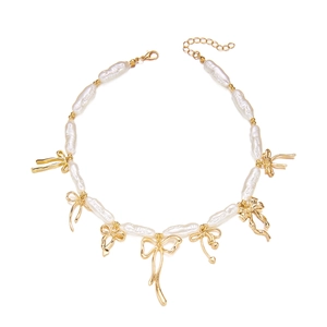Détail du collier de perles baroques avec pendentif nœud doré sur un fond blanc neutre